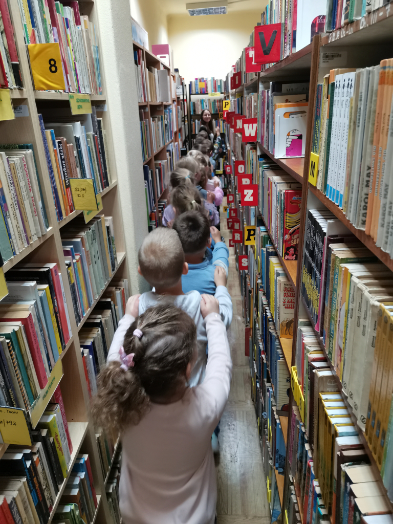 Pięcio i sześciolatki zwiedzające bibliotekę bawiące się w zabawę Wesoły pociąg
